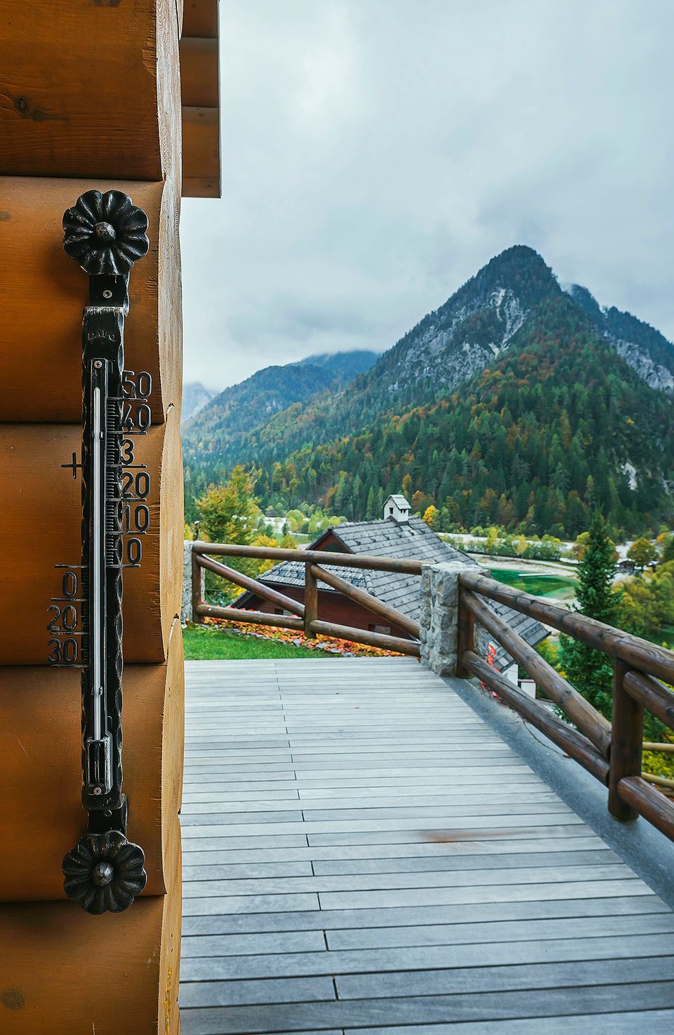 A balcony rail with an old thermometer, with a mountain peak visible beyond.