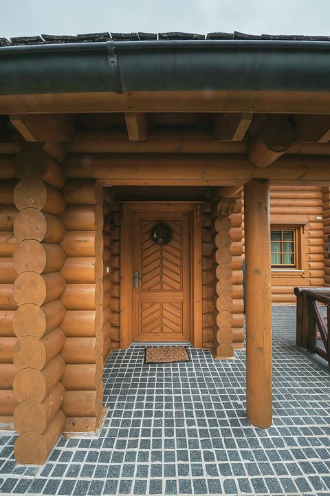 The chalet's carved timber front door set in a deep log-framed porch, with patterned stone paving underfoot.