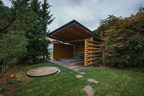 The garden with a lawn, stepping stones, a covered circular hot tub, and a timber-clad outdoor structure.