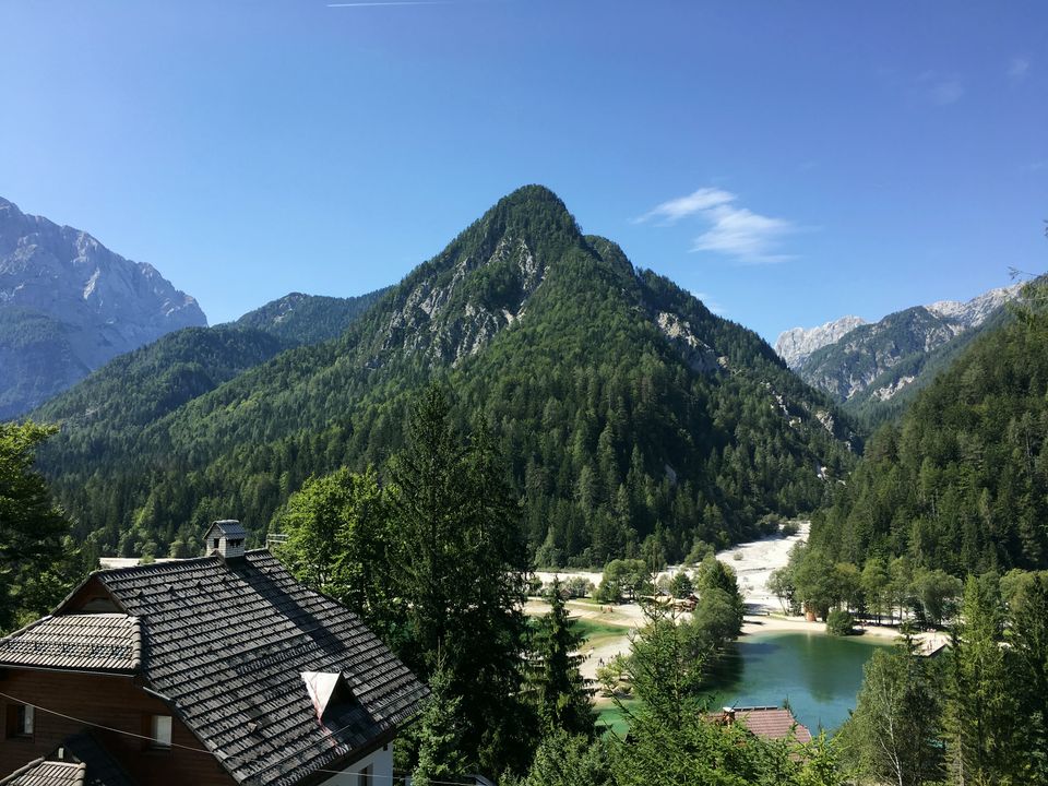 Lake Jasna in summer, its water turquoise below the forested slopes, with the shingle roof of the chalet in the foreground.