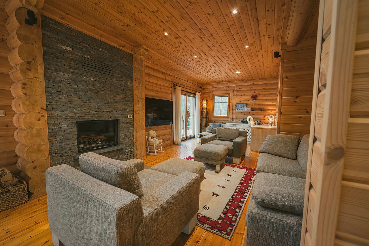 The living room with the stone fireplace lit, sofas, a TV, and round-log walls.