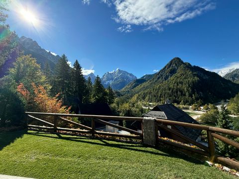 The lawn and timber railing in full sun, looking across to the snow-dusted peaks of the Julian Alps under a clear blue sky.