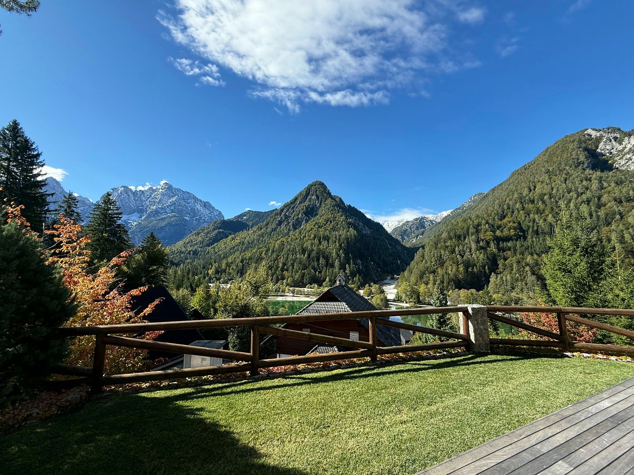 The view from the terrace on a clear day: lawn, timber railing, the valley below and Lake Jasna showing green between the trees.